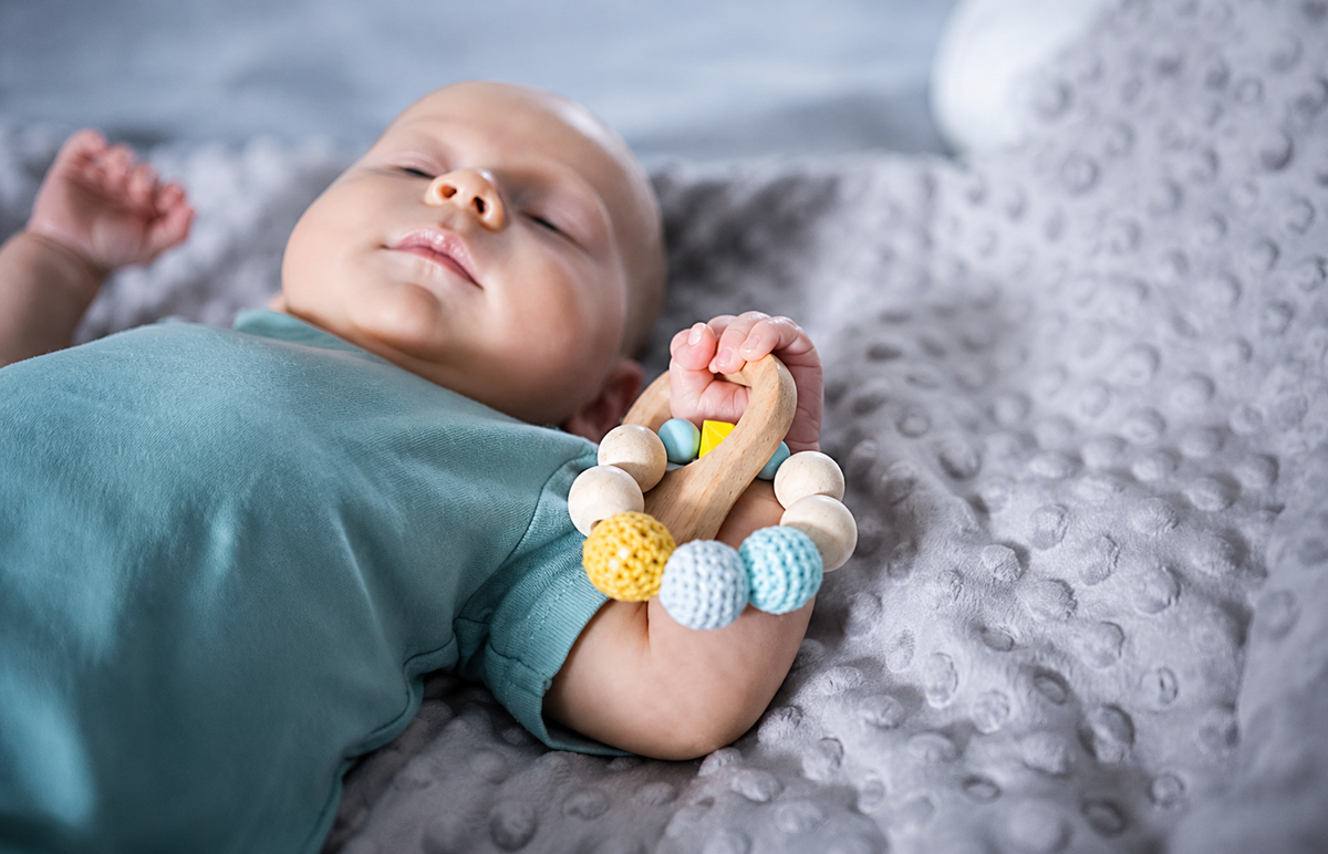 Bébé endormi tenant un hochet de dentition en bois et crochet